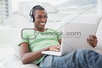 Smiling Afro man with headphones using laptop on sofa
