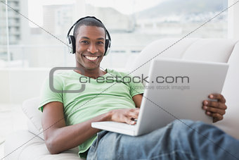 Portrait of smiling Afro man with headphones using laptop on sofa
