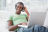Smiling young Afro man with headphones using laptop on sofa