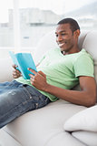 Side view of smiling Afro man reading a book on sofa