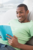 Side view of smiling Afro man reading a book on sofa