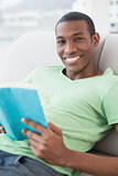 Portrait of smiling Afro man reading book on sofa