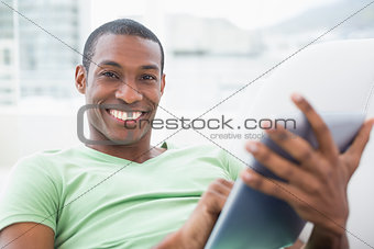 Casual smiling Afro man using digital tablet on sofa