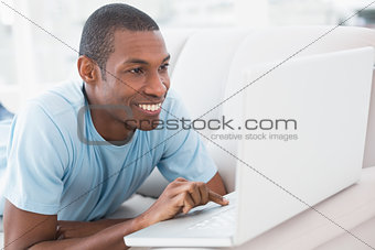 Relaxed casual Afro man with laptop lying on sofa