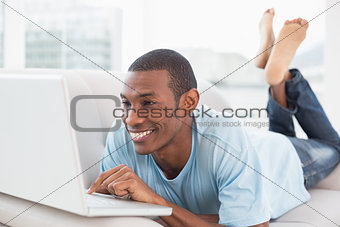 Relaxed casual Afro man with laptop lying on sofa