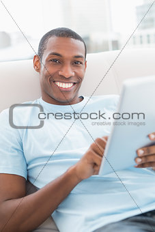 Casual smiling young Afro man using digital tablet on sofa