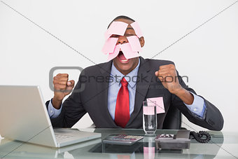 Frustrated Afro businessman with blank notes on face and laptop