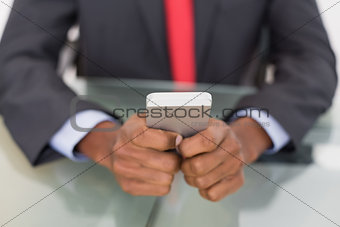 Mid section of well dressed businessman text messaging