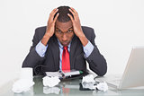 Frustrated Afro businessman with head in hands at  desk