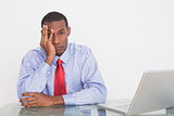 Angry Afro businessman with hand on face at desk