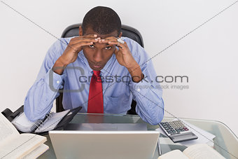 Afro businessman with head in hands at desk