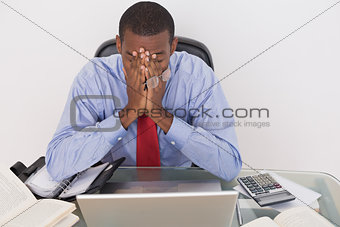 Angry Afro businessman with hands on face at desk