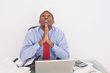 Afro businessman looking up with joined hands at desk