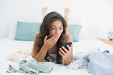 Shocked woman looking at mobile phone in bed