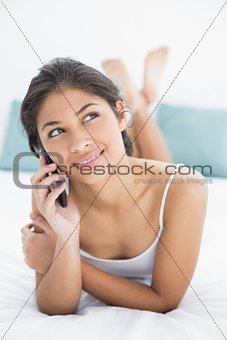 Thoughtful woman using mobile phone in bed