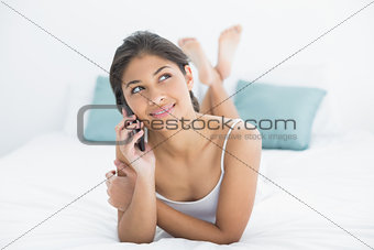 Thoughtful woman using mobile phone in bed