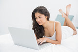 Concentrated casual woman using laptop in bed