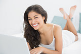 Cheerful casual young woman using laptop in bed