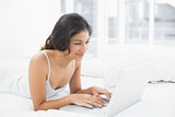 Smiling casual young woman using laptop in bed