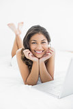 Smiling casual young woman with laptop in bed