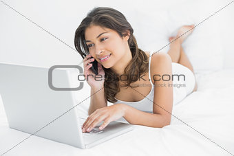 Casual woman using laptop and cellphone in bed