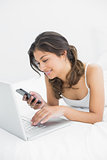 Casual woman using laptop while text messaging in bed