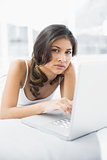 Serious casual woman using laptop in bed