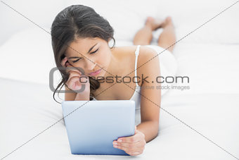 Thoughtful woman using tablet PC in bed