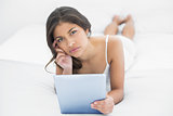 Serious casual woman using tablet PC in bed