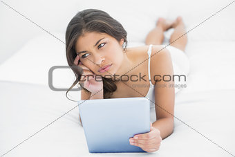 Thoughtful casual woman using tablet PC in bed