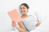 Cheerful woman reading a book in bed