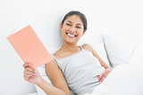 Cheerful young woman reading a book in bed