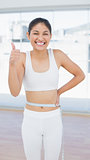Cheerful woman measuring waist while gesturing thumbs up