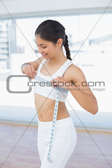 Smiling woman measuring chest in fitness studio