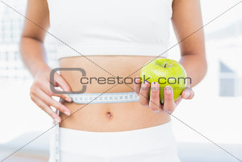 Mid section of woman measuring waist as she holds apple