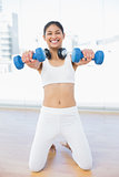 Cheerful woman exercising with dumbbells in fitness studio