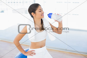 Woman drinking water while sitting on exercise ball
