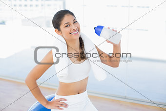 Woman on exercise ball with water bottle in fitness studio