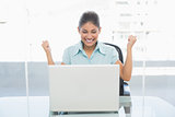 Happy businesswoman clenching fists in front of laptop