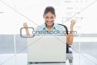 Happy businesswoman clenching fists in front of laptop