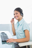 Cheerful businesswoman wearing headset while using computer