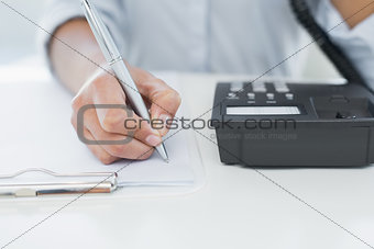 Mid section of woman using telephone while writing on clipboard