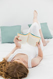 Relaxed young woman reading a book in bed