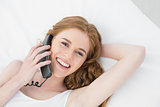 Cheerful young woman using telephone in bed