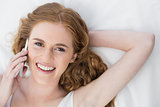 Cheerful young woman using mobile phone in bed