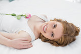 Pretty young woman resting in bed with a rose