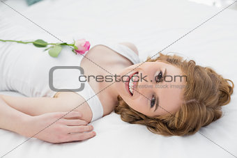 Pretty young woman resting in bed with a rose