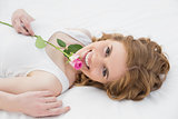 Pretty young woman resting in bed with rose