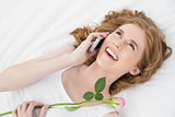 Woman using mobile phone while resting in bed with rose