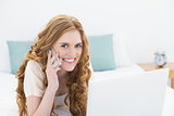 Portrait of smiling casual woman using laptop and cellphone in bed